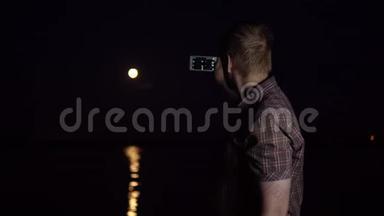 一个年轻人正在用智能手机<strong>相机</strong>拍摄一个红色的<strong>月亮</strong>。